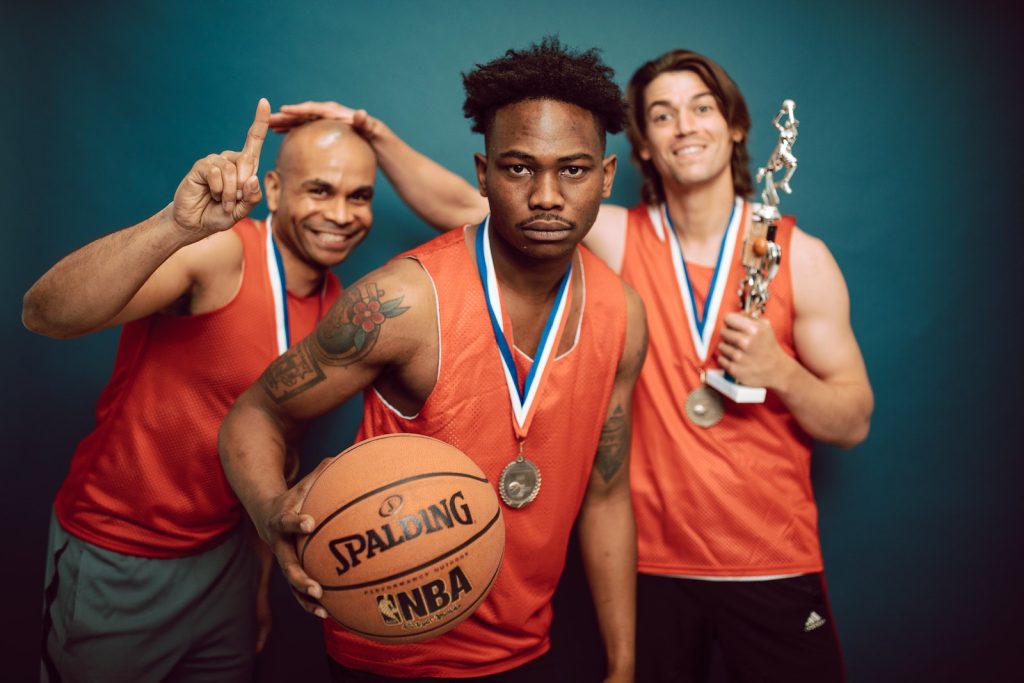 Three Men in Orange Jersey Shirt Holding Basketball and Trophy's.