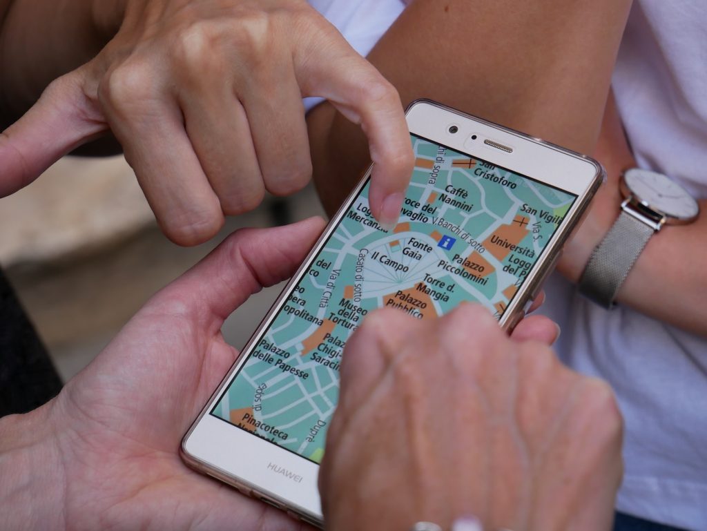 person touching smartphone with a map app and another person is pointing at a location.