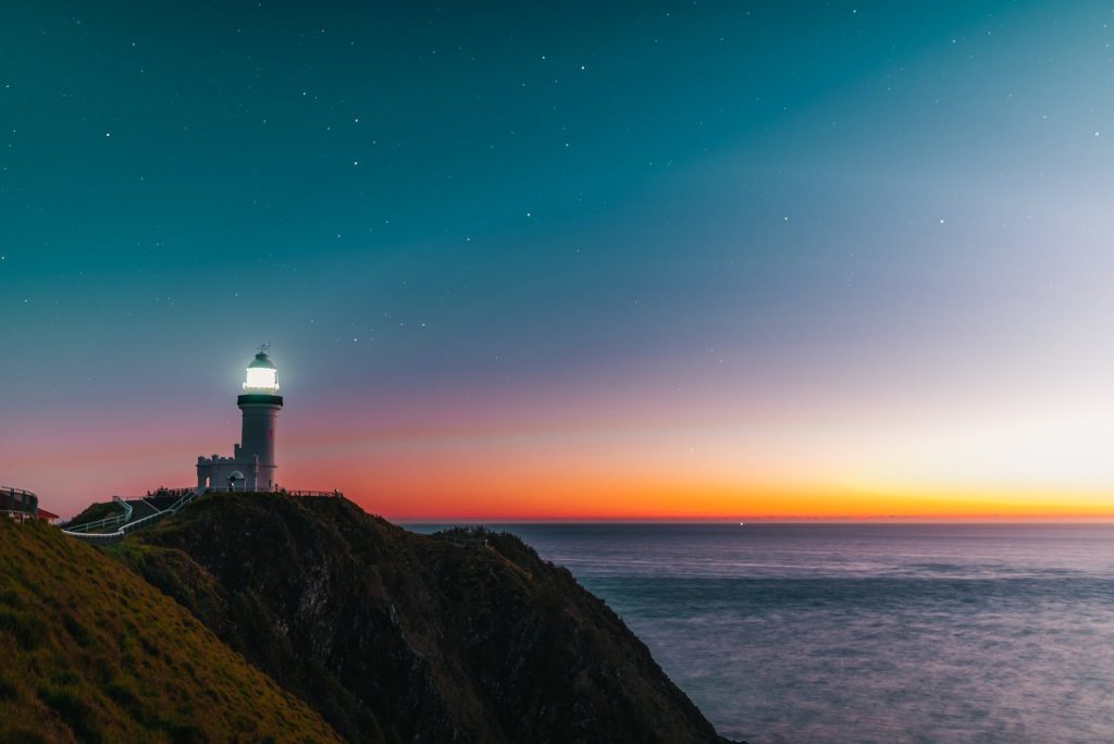 Amazing scenery of lighthouse tower located on rocky cliff against starry sunset sky over wavy ocean
