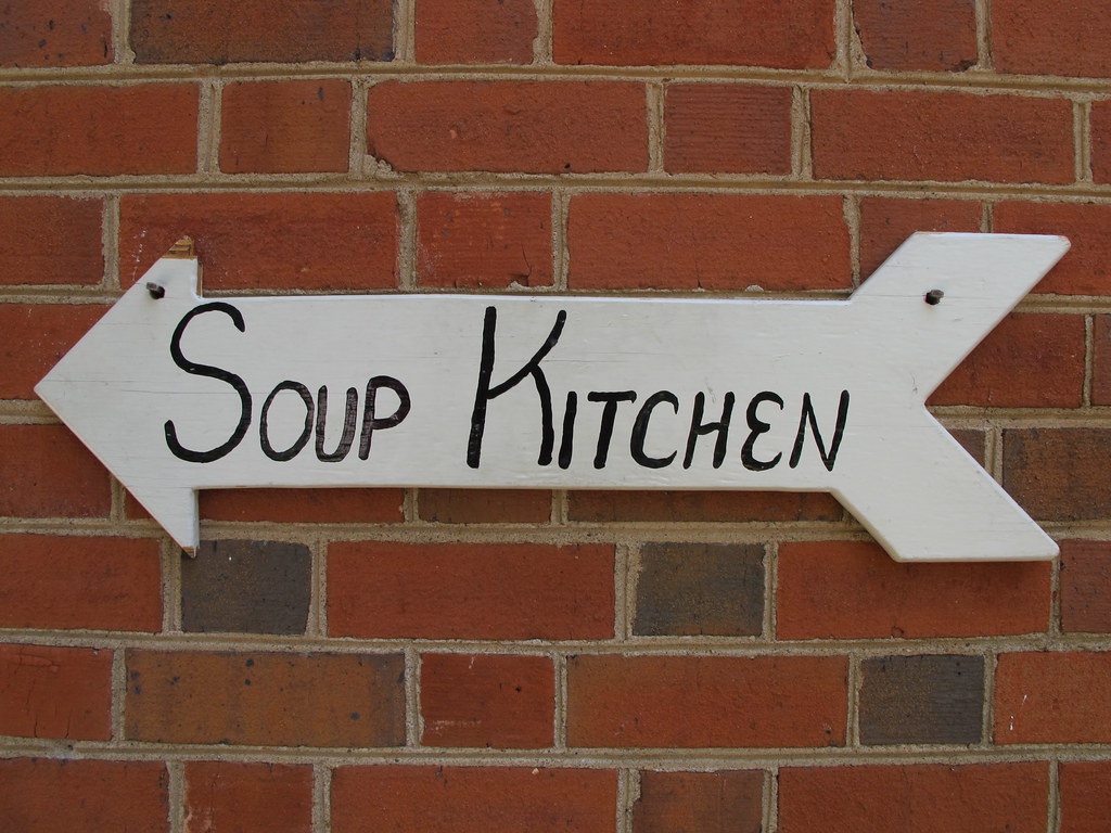 White, arrow shaped sign which reads: "Soup Kitchen".