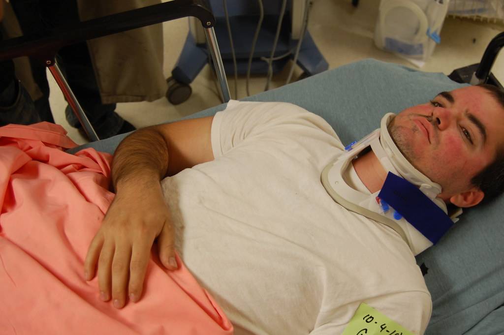 Man in hospital bed wearing a neck brace.