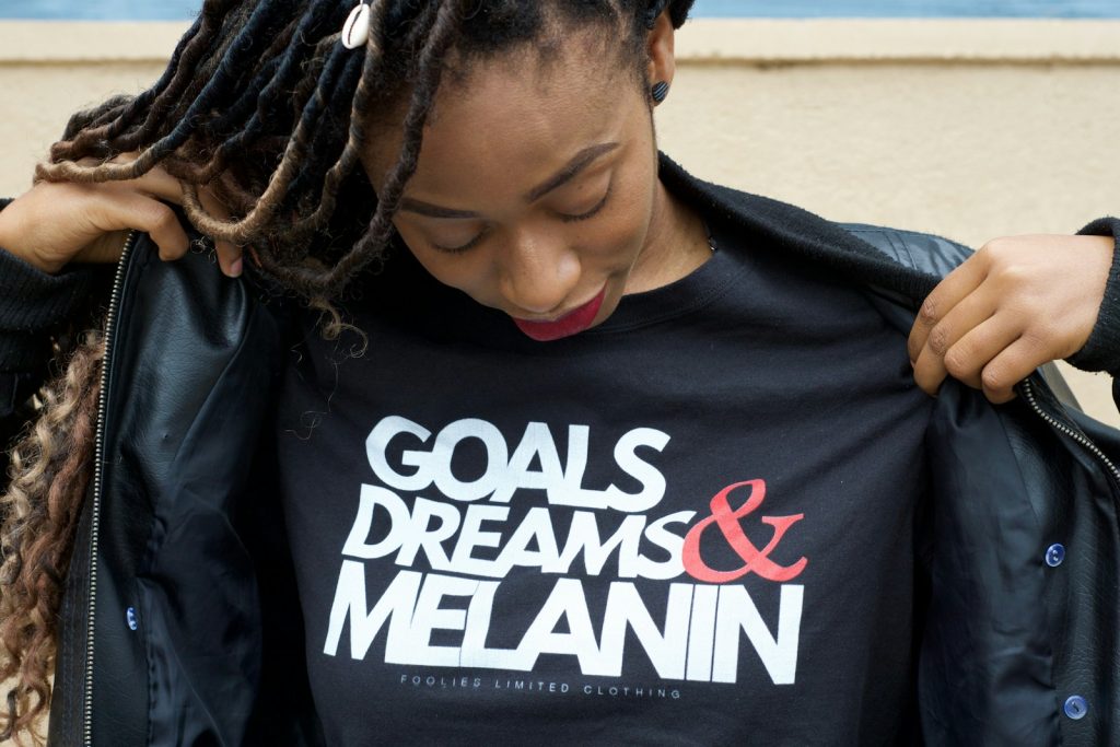 young lady holding up tshirt which reads; Goals Dreams & melanin.